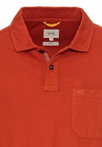 Rød økologisk bomulds polo-shirt med krave, tre sorte knapper, brystlomme og stikninger. Glat tekstur, afslappet design.