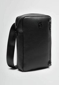 Borsa in pelle nera con texture, dalla forma rettangolare, dotata di tasca frontale con zip, tracolla regolabile e dettaglio del logo.