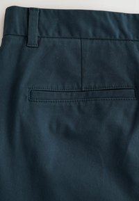 Pantalon bleu canard en tissu lisse et texturé. Dispose d'une poche passepoilée au dos et de passants de ceinture, structuré avec un design ajusté.