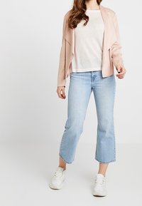 Ljusrosa, draperad jacka över en vit topp, i kombination med ljusblå caprijeans och vita träningsskor. Slät tygkvalitet och avslappnad passform.