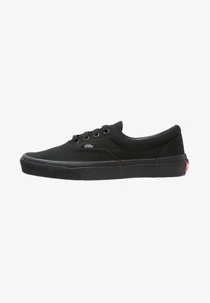 Sneaker nera in tela con lacci, design a basso profilo, suola in gomma e un piccolo logo bianco sul lato. Presenta una superficie liscia e uno stile minimalista.