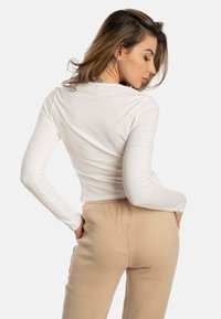 Camiseta blanca de manga larga, ajustada y hecha de tela suave, combinada con pantalones de cintura elástica beige, textura suave, diseño simple y sin patrones visibles.