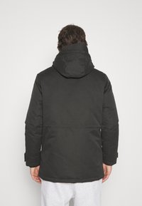 Schwarze Kapuzenjacke mit glatter Textur, gerade geschnitten, verstellbaren Bündchen und mittellangem Design. Schlichter, minimalistischer Stil.