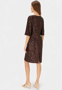Sukienka z brązowymi cekinami z krótkimi rękawami, z rozcięciem z tyłu i gładką fakturą. W połączeniu z jasnymi, masywnymi obcasami.