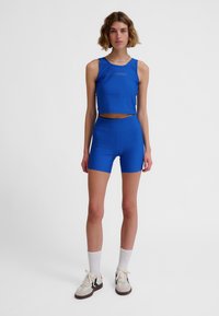 Blå träningsset med ett kort linne och höga shorts. Slät tyg med en figurnära silhuett och en diskret logga på bröstet.