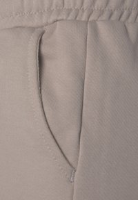 Light gray fabric with a smooth texture features a side pocket and elastic waistband. Fine stitching is visible along the edges.