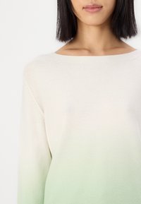 Pull en maille crème clair avec un dégradé qui s'estompe vers un doux vert. Il présente un col large et un tissu texturé, mettant en valeur une coupe décontractée.