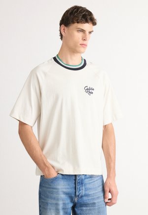 Beige short-sleeve t-shirt with a ribbed navy and green neckline, featuring a small blue logo on the left chest. Casual, relaxed fit.