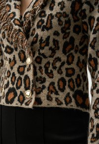Maglione corto con stampa leopardata in toni neutri, caratterizzato da bottoni esagonali dorati e bordi sfilacciati. Realizzato in un tessuto morbido e testurizzato.