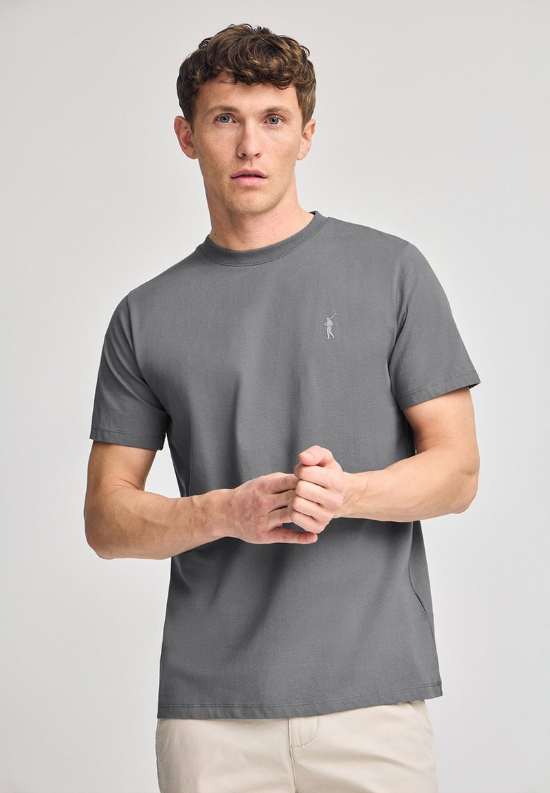 Grå bomullströja med rund hals, korta ärmar och en liten broderad design på bröstet. Slingerande textur, avslappnad passform.