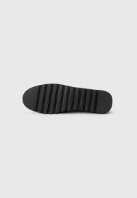 Talpa de cauciuc negru cu striatii orizontale și nervuri, având un vârf rotunjit și un logo de marcă embosat aproape de călcâi.