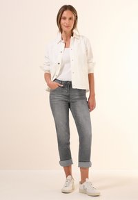 Chaqueta de mezclilla blanca sobre una camiseta blanca, combinada con unos jeans grises recortados y enrollados en los puños, y zapatillas blancas con un toque de color sutil.