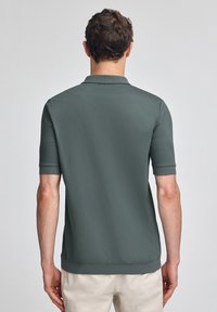 Pikétröja i mörkgrön tyg, korta ärmar och ribbad krage. Slät textur med en något figursydd form och utan synliga logotyper.