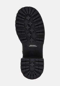 Suela negra de una bota Guess, talla 37, con profundas ranuras y patrones en forma de cruz, etiquetada "Hecho en China" y "Muestra no para reventa."