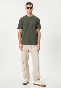 Olivengrønt kortærmet T-shirt parret med beige cargobukser med cargolommer, båret med hvide sneakers med brune såler og sorte solbriller.