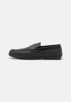 Mocassins noirs avec un tissu texturé arborant un motif subtil, une bride en cuir lisse sur le dessus, et une semelle en caoutchouc flexible.