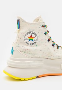 High-top white canvas Converse sneakers with multicolored speckles, featuring a logo patch, colorful laces, and a vibrant rubber sole.