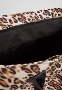 Sac en léopard ouvert, montrant un revêtement intérieur en tissu noir et une fermeture éclair argentée visible le long du bord supérieur.