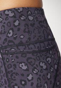 Aukštai liemeniui pritaikytos legginsai tamsiai purpurnės spalvos audiniu su juodu leopardų raštu. turi plokščių siūlių ir užpakalinę kišenę.