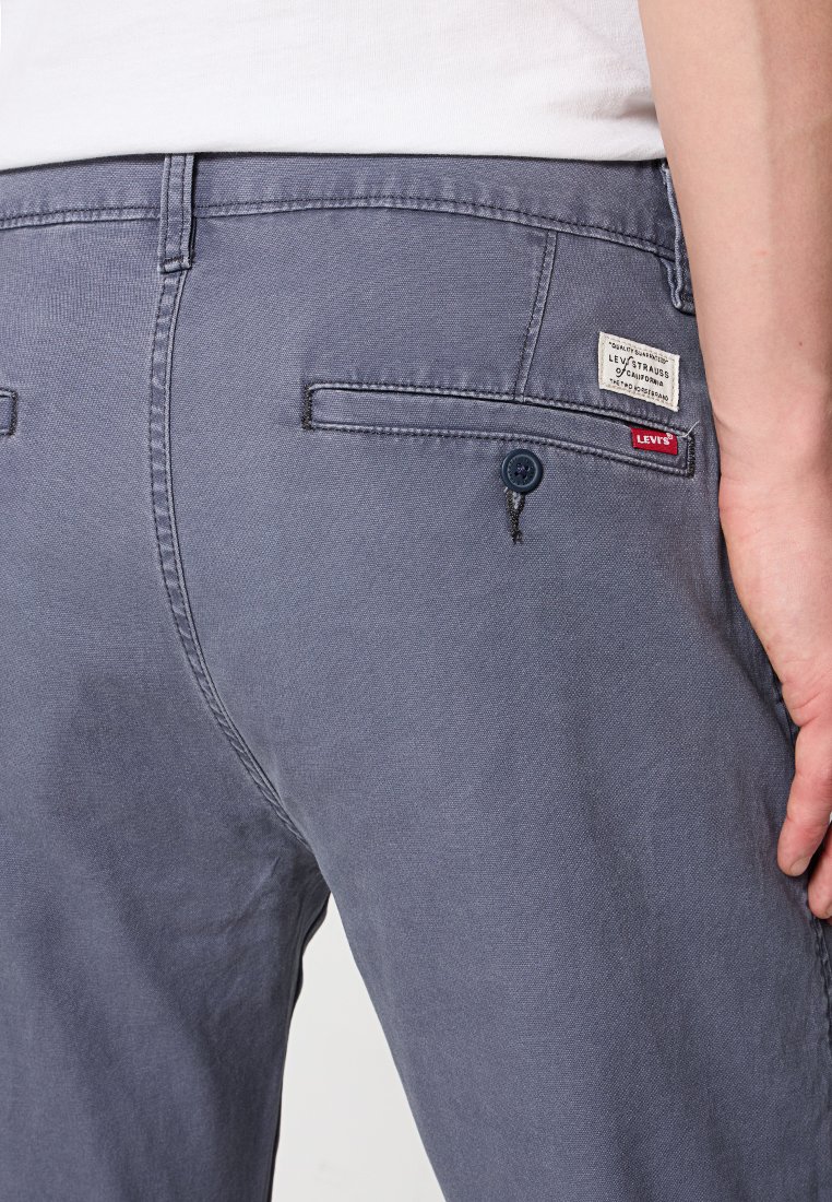 Pantalones de algodón grises con una textura suave, que cuentan con dos bolsillos traseros, una etiqueta en el bolsillo derecho y un detalle de botón.