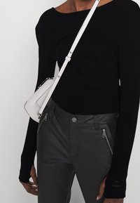 Black ribbed long-sleeve top paired with fitted dark gray pants featuring zippers, and a small white crossbody bag with silver hardware.