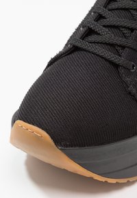 Musta urheilukenkä, jossa verkkokangas päällisessä, teksturoitu pinta, mustat nauhat ja kumipohja. Pyöristetty kärki ja kevyesti pehmustettu sisäpohja.