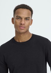 Must mustriga sviiter ümarate kaelustega. Sujuv tekstuur, kehaõhuke disain ja minimalistlik stiil ilma mustriteta või nähtava riistvarata.