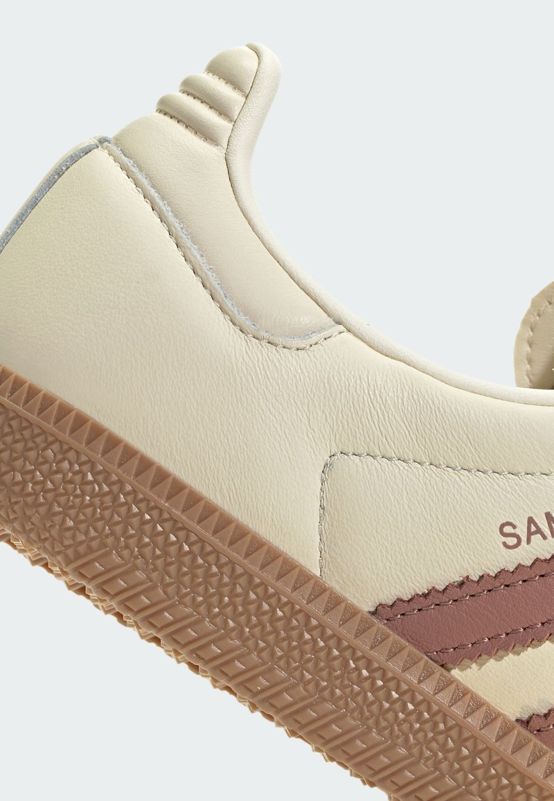 Krämfärgad sneaker med en texturerad gummisula, som har en rosa accentrand, slät läderövre och ribbad häldetalj.