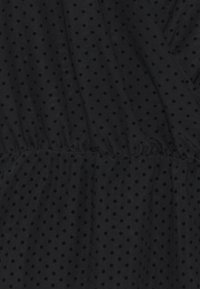 Black fabric with small, textured black polka dots. Features gathered waistband and flowing design, creating a soft drape.