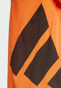 Tela de malla naranja con patrones geométricos negros que presenta un acabado texturizado. Diseñada para la visibilidad con colores contrastantes y formas audaces.