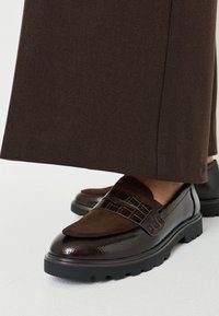 Braune Leder-Loafers mit strukturiertem Wildleder und glatten Akzenten, ausgestattet mit einem gemusterten Band und einer massiven schwarzen Gummisohle.
