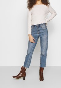 Pull à manches longues beige clair, jean bleu taille haute, et bottines marron embossées effet crocodile avec talon bloc.