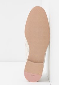 Semelle de chaussure beige avec texture à motifs, dessous en caoutchouc rose clair, marqueur de taille doré (37) et logo embossé. Design plat avec accents minimalistes.