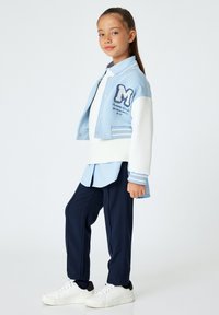Lichtblauwe cropped varsityjack met witte mouwen, marineblauwe broek en witte sneakers. Heeft geborduurde letters en strepen.