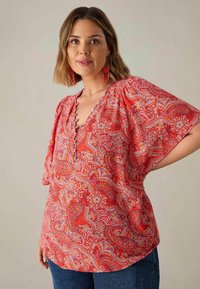 Rote Bluse mit Paisleymuster, kurzen Fledermausärmeln, V-Ausschnitt und dekorativen Knöpfen. Der Stoff hat eine glatte Textur mit lebhaften Akzenten.