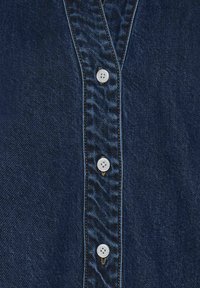 Camicia in denim blu scuro con chiusura a bottoni sul davanti, cinque bottoni bianchi visibili, cuciture a vista e tessuto testurizzato.