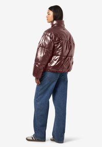 Blizgi tamsiai raudona pūsta striukė su aukštu apykakliu, su siūtomis dalimis ir laisvo silueto, derinama su šviesiai mėlynais plačiomis kelnėmis.