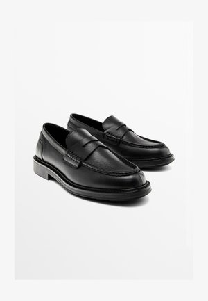 Black leather loafers with a rounded toe, decorative stitching, and a strap across the vamp. Flat rubber sole, smooth texture.