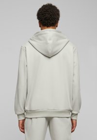 Lysgrå hoodie med en stor, rund hætte, ribbede manchetter og nederkant samt en glat overflade. Simpelt design uden synlige logoer eller mønstre.