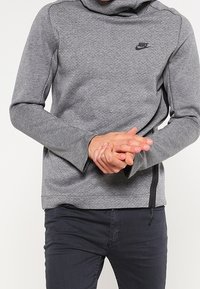 Grå Nike sweatshirt med hög krage, långa ärmar och en subtil textur. Har en liten svart logga på bröstet och sidodragkedja.