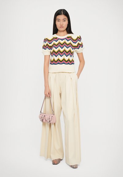 Pull crème clair avec un motif en zigzag coloré, manches ballon ; pantalon beige à jambes larges ; petit sac à main rose ; chaussures rayées multicolores.