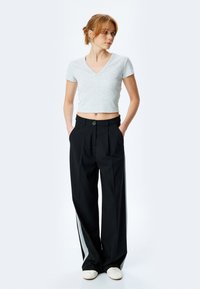 Grå kortærmet t-shirt med V-hals parret med sorte wide-leg bukser med en sidelæns stribe og en frontlukning med knap.