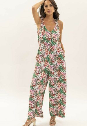 Femme portant une combinaison sans manches à jambes larges avec un motif abstrait multicolore vert, rouge et rose, posant avec une main sur la tête.