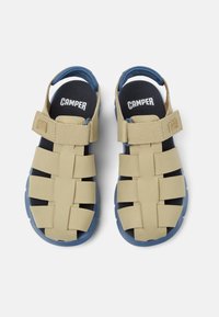 Brązowe sandały z niebieskimi akcentami, z paskiem i zapięciem na rzep. Cholewka ma warstwowy design z szerokimi wycięciami i teksturowaną podeszwą.