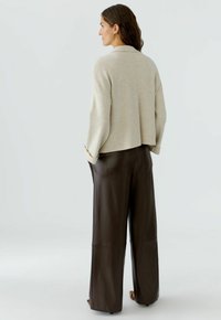 Beige, verkorte trui met een relaxte pasvorm en lange mouwen, gecombineerd met high-waisted, donkerbruine leren wijdpijpkousen.