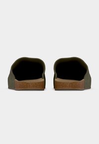 Πράσινα παπούτσια slip-on με στρογγυλεμένο πίσω μέρος, εξωτερική σόλα τύπου φελλού και υφασμένο πάνω μέρος, που παρουσιάζουν μινιμαλιστικό στυλ.