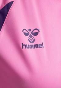 Purple hummel logo and text on pink fabric with a small visible purple fabric section at the top left corner.