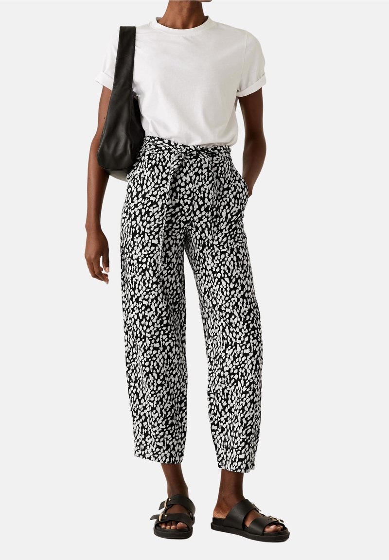 Schwarz-weiß gemusterte Hose mit lockerer Passform, mit einem Bindegürtel, Seitentaschen, kombiniert mit einem schlichten weißen T-Shirt und schwarzen Sandalen.