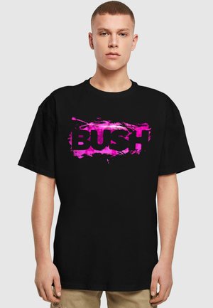 Sort bomulds T-shirt med stort pink "BUSH" tekst og en tekstureret splatter-effekt. Korte ærmer og afslappet pasform.