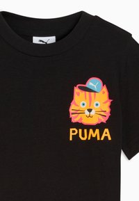 Crna majica s kratkim rukavima s živopisnim crtanjem tigra koji nosi plavu Puma kapu iznad žutog natpisa "PUMA" na prsima.